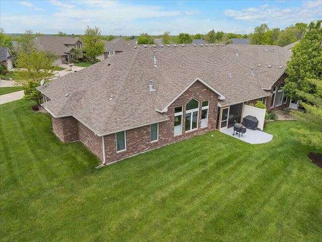 back of property featuring a lawn, a patio, roof with shingles, and brick siding