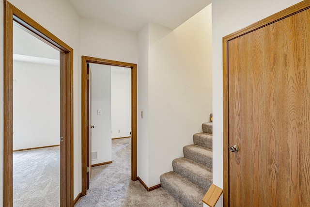 corridor with baseboards, stairway, visible vents, and light colored carpet