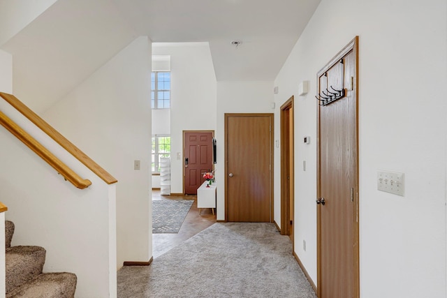 hallway with light carpet, baseboards, a towering ceiling, and stairs