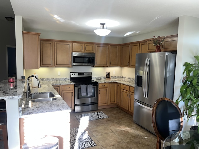 kitchen featuring stainless steel appliances, a sink, a peninsula, light stone countertops, and tile patterned flooring