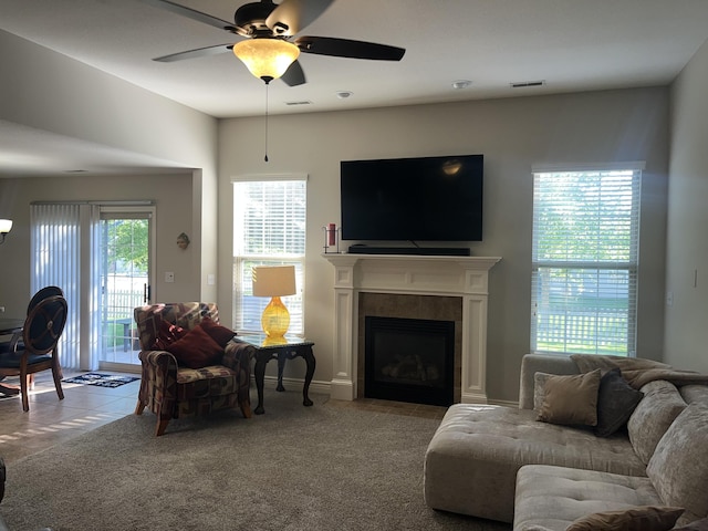 living area with a ceiling fan, tile patterned flooring, a tiled fireplace, and carpet