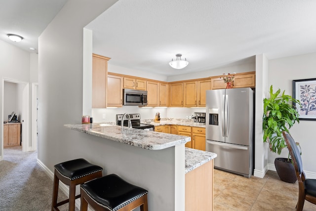 kitchen featuring appliances with stainless steel finishes, a peninsula, a kitchen breakfast bar, light stone counters, and baseboards