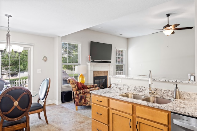 kitchen with a sink, stainless steel dishwasher, open floor plan, light tile patterned flooring, and light stone countertops