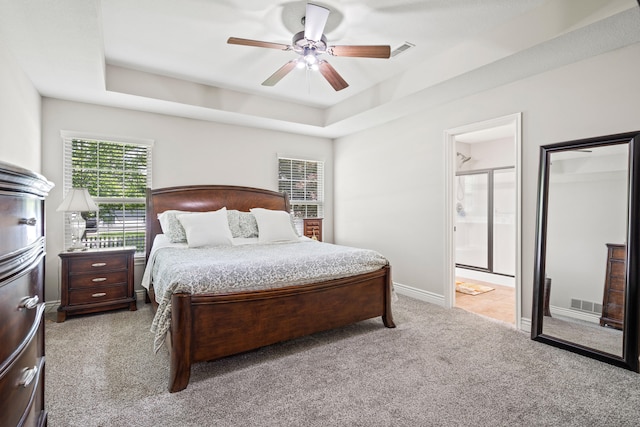 carpeted bedroom featuring a raised ceiling, a ceiling fan, ensuite bathroom, and baseboards
