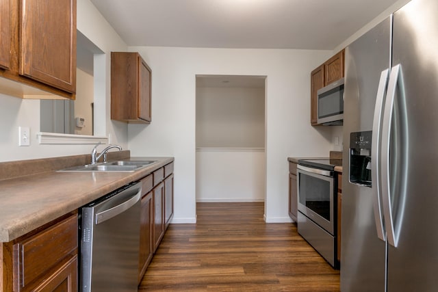 kitchen featuring appliances with stainless steel finishes, a sink, dark wood-style floors, brown cabinetry, and baseboards