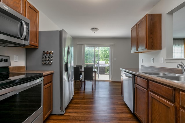 kitchen with stainless steel appliances, a sink, dark wood-type flooring, and brown cabinets