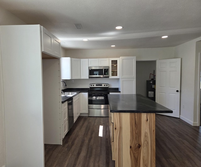 kitchen featuring appliances with stainless steel finishes, water heater, dark countertops, dark wood-type flooring, and recessed lighting