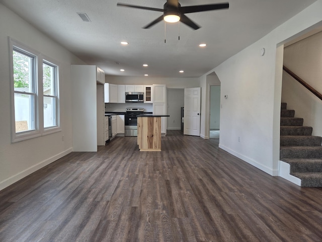 kitchen with appliances with stainless steel finishes, open floor plan, dark countertops, dark wood-type flooring, and recessed lighting