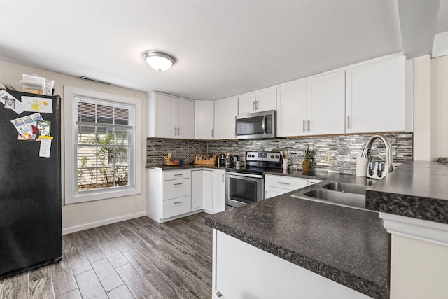 kitchen with a sink, backsplash, dark countertops, stainless steel appliances, and white cabinets