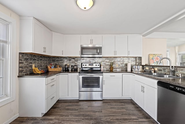 kitchen featuring a sink, dark countertops, stainless steel appliances, white cabinetry, and tasteful backsplash
