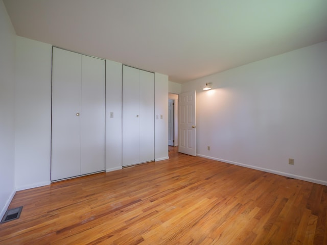unfurnished bedroom featuring two closets, light wood-style floors, and baseboards