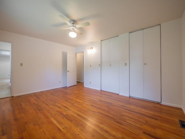 unfurnished bedroom with multiple closets, light wood-type flooring, baseboards, and ceiling fan