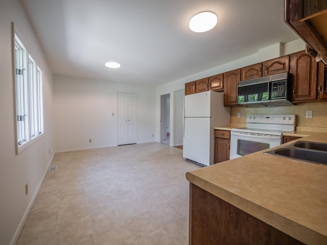 kitchen with white appliances, baseboards, light countertops, and a sink