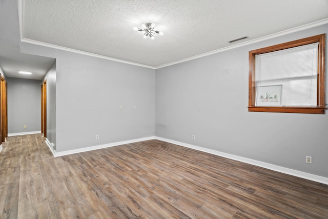 empty room with a textured ceiling, wood finished floors, ornamental molding, and baseboards