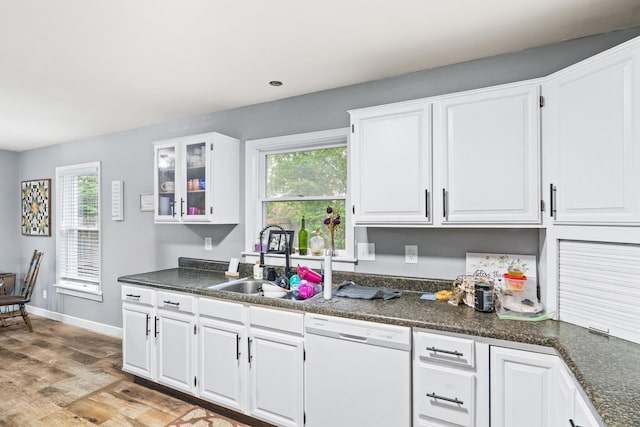 kitchen featuring white dishwasher, light wood-type flooring, dark countertops, white cabinetry, and a sink