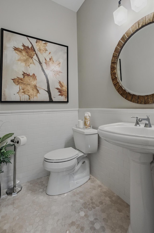 bathroom with toilet, wainscoting, tile walls, and a sink