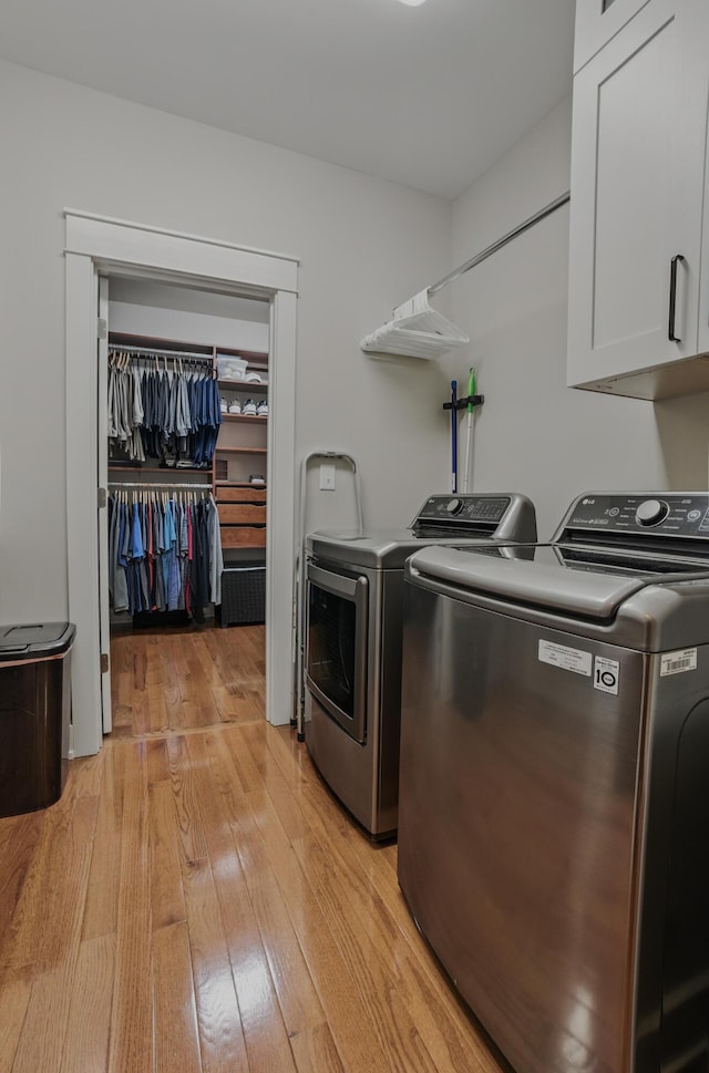 clothes washing area with cabinet space, washing machine and clothes dryer, and light wood-style flooring