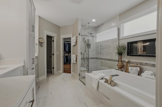 full bath with a shower stall, a garden tub, vanity, marble look tiles, and a spacious closet