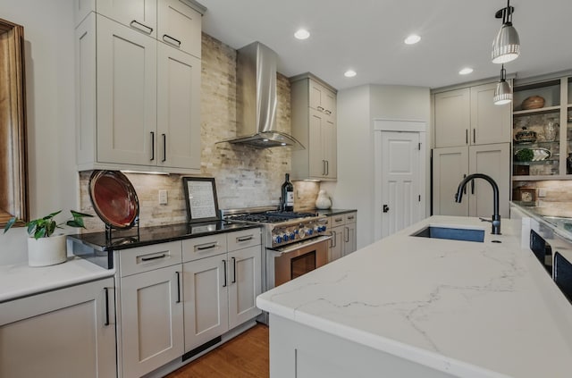 kitchen with wall chimney range hood, a sink, high end stainless steel range oven, pendant lighting, and decorative backsplash