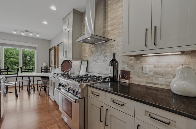 kitchen with wall chimney exhaust hood, high end stainless steel range oven, dark stone countertops, backsplash, and recessed lighting