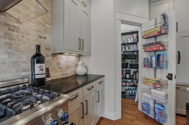 kitchen featuring gas range, backsplash, wood finished floors, and dark stone countertops