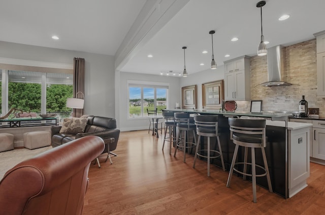 kitchen featuring wall chimney range hood, open floor plan, light wood-style flooring, decorative backsplash, and recessed lighting