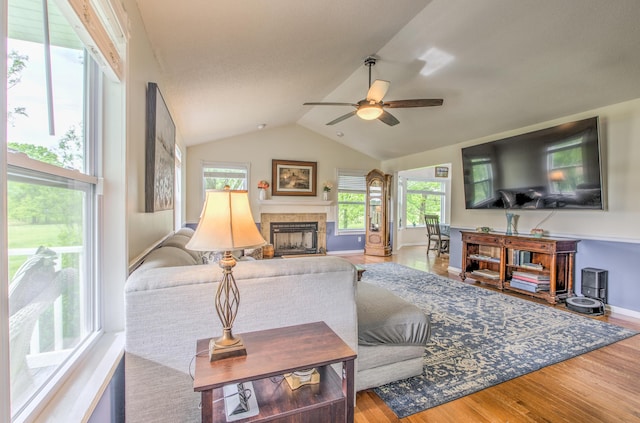 living area featuring a ceiling fan, wood finished floors, a tile fireplace, vaulted ceiling, and baseboards
