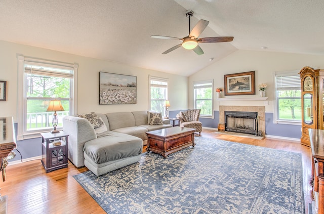 living area featuring ceiling fan, light wood-type flooring, a tile fireplace, lofted ceiling, and baseboards