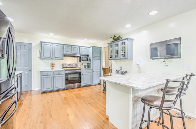 kitchen featuring appliances with stainless steel finishes, a peninsula, a breakfast bar area, glass insert cabinets, and light countertops
