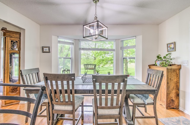 dining area featuring plenty of natural light, light wood-style floors, a chandelier, a textured ceiling, and baseboards