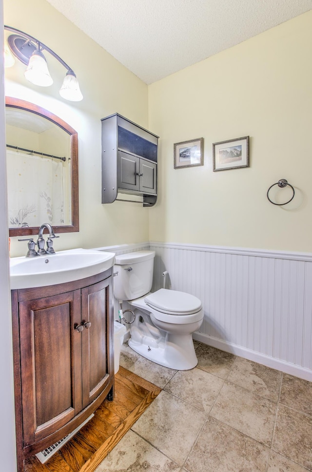 full bathroom with toilet, wainscoting, vanity, tile patterned floors, and a textured ceiling