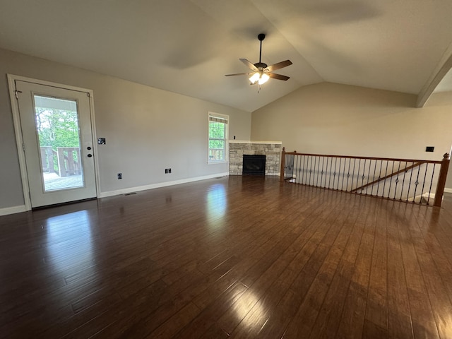 unfurnished living room with ceiling fan, dark wood finished floors, lofted ceiling, baseboards, and a stone fireplace