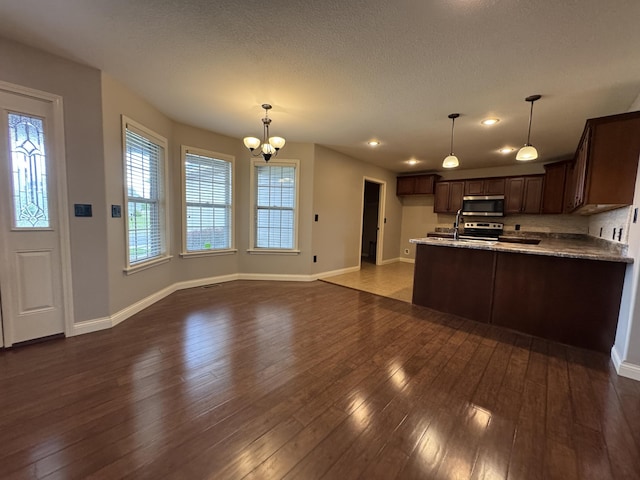kitchen featuring stainless steel appliances, baseboards, dark brown cabinetry, a chandelier, and dark wood-style flooring
