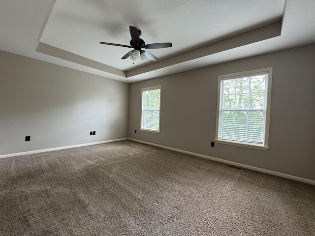 carpeted spare room with a raised ceiling, baseboards, and ceiling fan