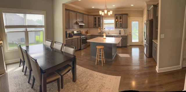 kitchen with appliances with stainless steel finishes, under cabinet range hood, a chandelier, a kitchen island, and backsplash