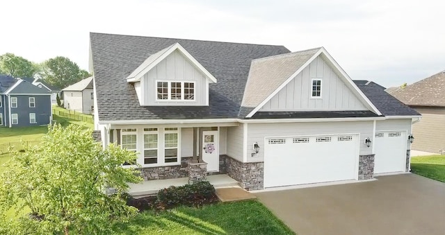 view of front of property with board and batten siding, driveway, stone siding, a porch, and roof with shingles
