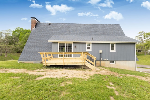 back of property with a chimney, a wooden deck, roof with shingles, and a lawn