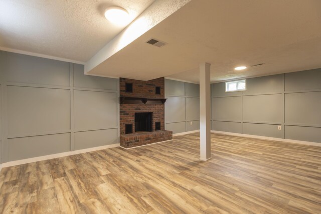 basement with a decorative wall, wood finished floors, a textured ceiling, and a brick fireplace