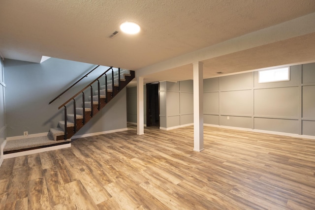 basement with wood finished floors, stairway, a textured ceiling, and baseboards