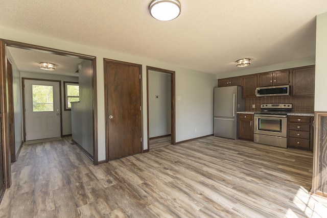 kitchen featuring stainless steel appliances, decorative backsplash, light countertops, wood finished floors, and dark brown cabinets