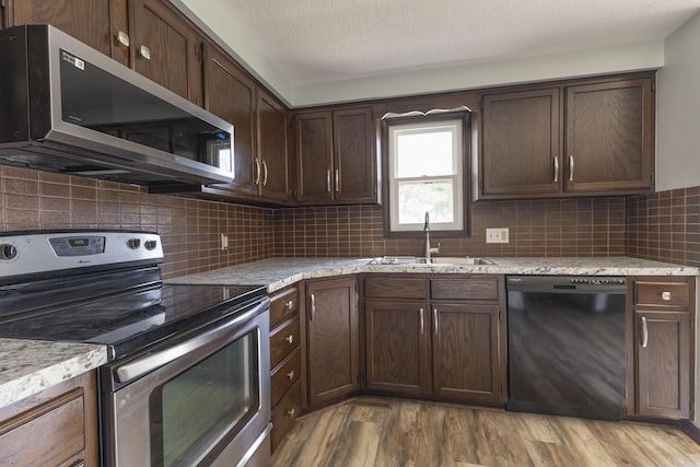 kitchen with stainless steel appliances, a sink, wood finished floors, dark brown cabinetry, and tasteful backsplash