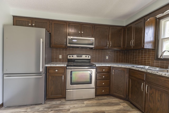 kitchen with stainless steel appliances, a sink, tasteful backsplash, dark brown cabinets, and a textured ceiling