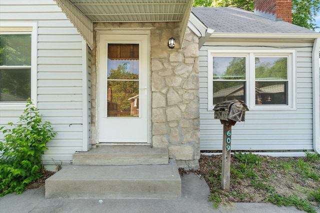 property entrance with a chimney, roof with shingles, and stone siding