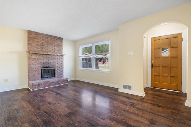 unfurnished living room with wood finished floors, baseboards, a brick fireplace, and arched walkways