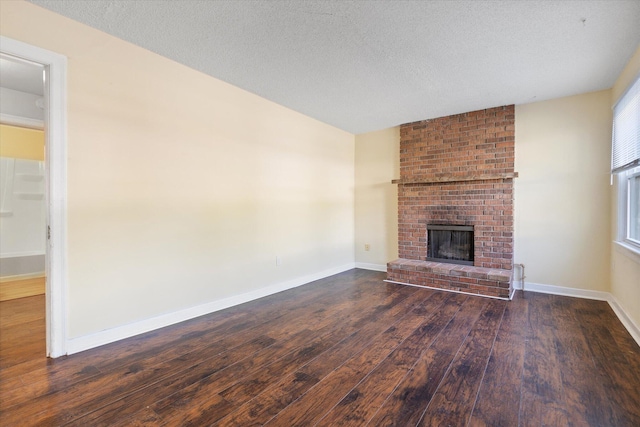 unfurnished living room featuring dark wood-type flooring, a brick fireplace, a textured ceiling, and baseboards