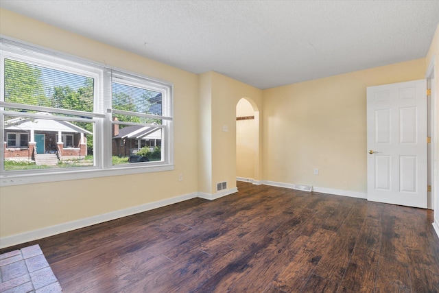 unfurnished room featuring wood finished floors, arched walkways, baseboards, and a textured ceiling