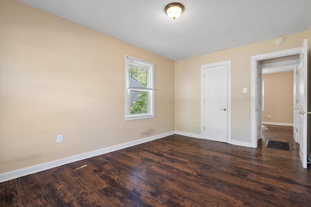unfurnished room featuring baseboards, dark wood finished floors, and a smoke detector