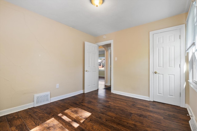 unfurnished bedroom featuring baseboards, wood finished floors, and arched walkways