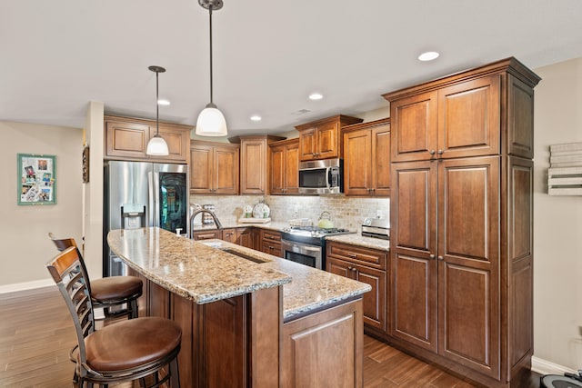 kitchen with stainless steel appliances, a sink, dark wood finished floors, light stone counters, and an island with sink