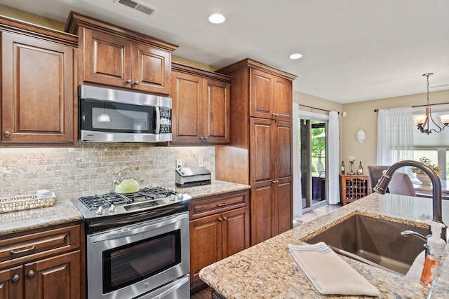 kitchen with appliances with stainless steel finishes, a sink, decorative backsplash, a chandelier, and pendant lighting